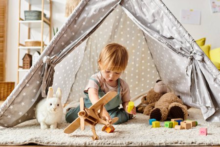 Photo for Toddler girl plays happily with toys inside a playful tent at home. - Royalty Free Image