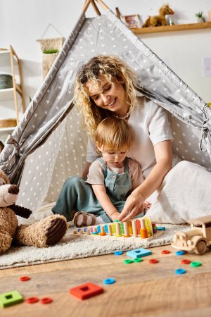 A curly-haired mother and her toddler daughter are happily playing inside a play tent using the Montessori method.