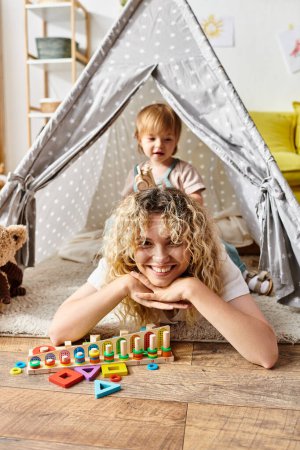 A curly-haired mother lying on the floor with her toddler daughter, exploring Montessori activities at home.
