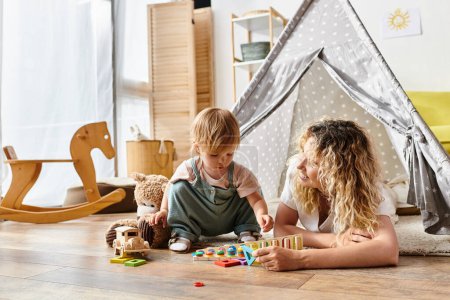 A curly-haired mother and her toddler daughter engage in imaginative play with educational toys, following the Montessori method.