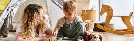 Eine lockige Mutter und ihre kleine Tochter üben sich in spielerischem Montessori-Lernen und kuscheln gemeinsam mit einem Teddybär.