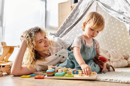 Photo for A curly-haired mother and her toddler daughter are happily playing with educational toys using the Montessori method at home. - Royalty Free Image