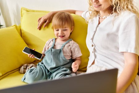 Photo for Curly mother and her toddler daughter sitting on a couch, engrossed in a laptop screen. - Royalty Free Image