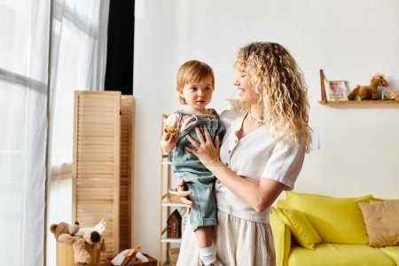 A curly-haired mother lovingly holds her toddler daughter in a cozy living room setting.