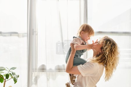 Téléchargez les photos : Curly mother tenderly embraces her toddler daughter at home, showcasing a beautiful bond of love and care. - en image libre de droit