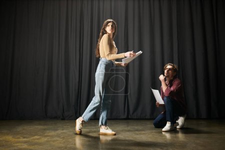Mujer de pie con gracia frente a una cortina negra durante los ensayos de teatro junto a su pareja.