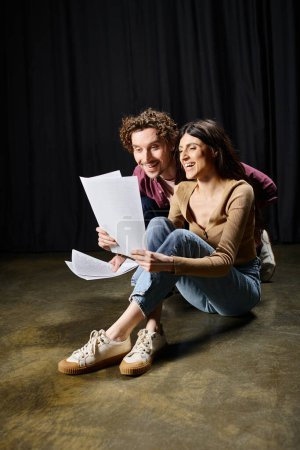 A man and woman share ideas while holding papers on the ground.