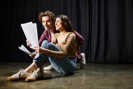 Homme et femme assis par terre, tenant des papiers, discutant du scénario du théâtre.