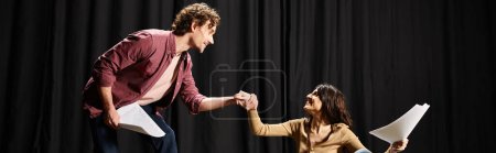 Foto de Handsome man and woman rehearse lines on stage, holding scripts. - Imagen libre de derechos