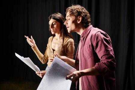 Man and woman hold paper, rehearsing in theater.