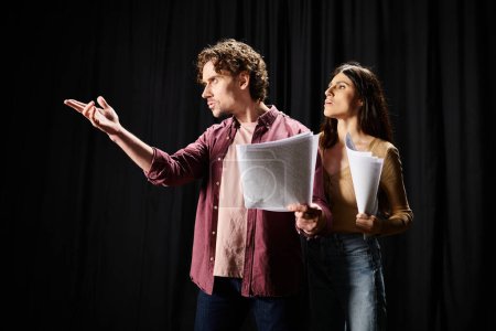 A man and woman rehearse together, holding papers.