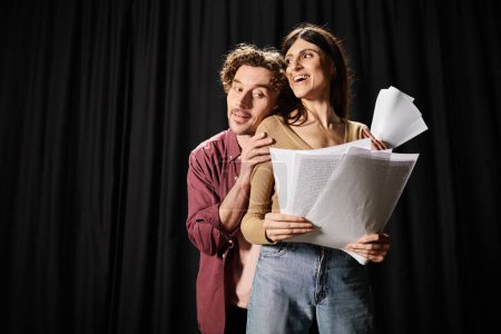 A man and woman collaborate, holding a paper during a theater rehearsal.