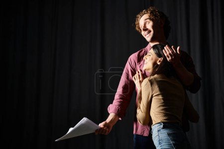 Foto de Un hombre y una mujer de pie ante una cortina negra, absortos en su actuación ensayada. - Imagen libre de derechos