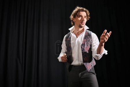 Foto de Hombre con estilo en camisa blanca y pantalones negros posa contra la cortina negra dramática. - Imagen libre de derechos