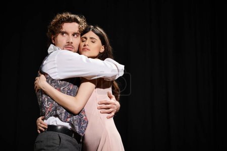 A man tenderly hugs a woman against a black background.