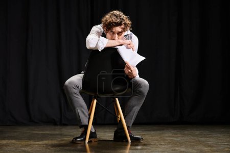 A man confidently sits atop a chair, holding a piece of paper.