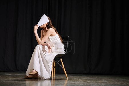 Anmutige Frau im weißen Kleid sitzt auf Stuhl.