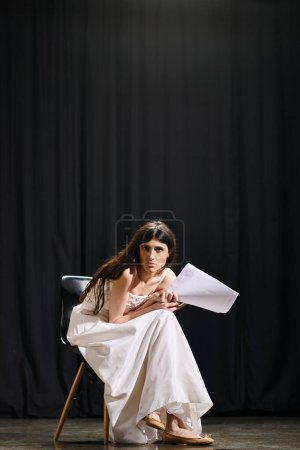 Une femme étonnante dans une robe blanche fluide assise gracieusement sur une chaise.