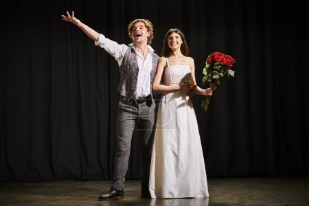 Un hombre y una mujer se paran elegantemente en un escenario de teatro durante los ensayos.