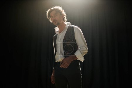 Foto de Un hombre guapo se para confiadamente frente a una cortina negra durante un ensayo de teatro. - Imagen libre de derechos