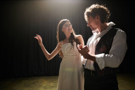 Téléchargez les photos : A woman in a white dress and a man in a black vest rehearse a performance in a theater. - en image libre de droit