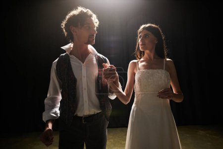 Un hombre y una mujer de pie en una habitación oscura, ensayando para el teatro.