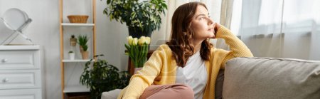 Photo for Middle-aged woman sitting on a couch, looking up thoughtfully. - Royalty Free Image