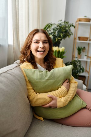 Photo for Middle-aged woman sitting on couch, cradling soft pillow. - Royalty Free Image