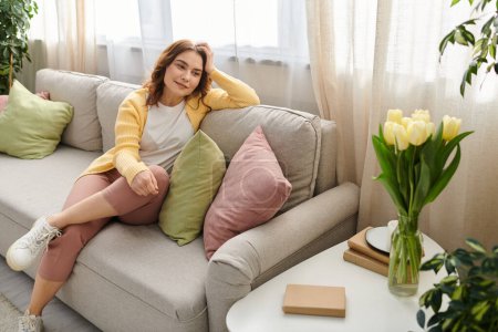 Middle aged woman sitting elegantly on a gray couch.