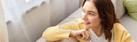 Photo for Middle aged woman in yellow sweater relaxes on a couch. - Royalty Free Image