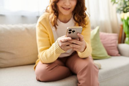 Middle-aged woman relaxes on couch, absorbed in cell phone.