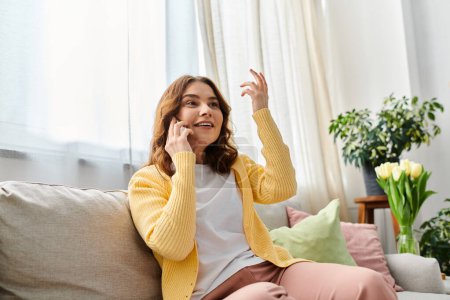 A beautiful middle-aged woman sitting on a couch, talking on a cell phone.
