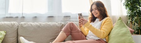 Photo for Middle-aged woman on couch engrossed in cellphone. - Royalty Free Image