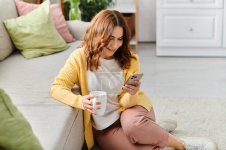 A middle aged woman engrossed in her cellphone while sitting on a couch.