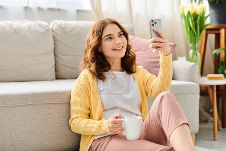 Photo for A middle aged woman sits on a couch, taking a selfie with her phone. - Royalty Free Image