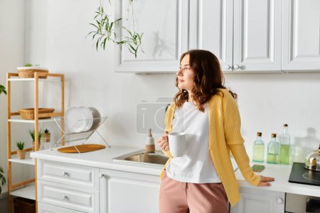 Middle-aged woman calmly standing in kitchen, holding cup.