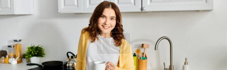 Frau mittleren Alters steht in Küche und hält Tasse.