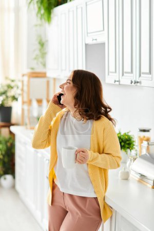 Photo for Middle aged woman standing in kitchen, chatting on cell phone. - Royalty Free Image