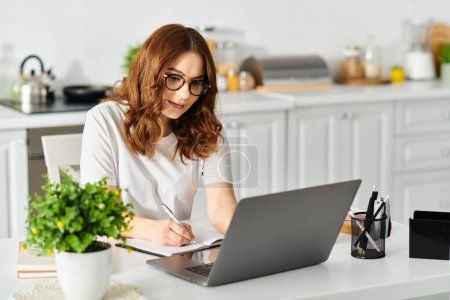 Foto de Middle-aged woman engrossed in laptop work at home table. - Imagen libre de derechos