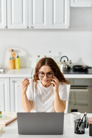 Photo for A middle-aged woman immersed in her work on a laptop at a kitchen table. - Royalty Free Image
