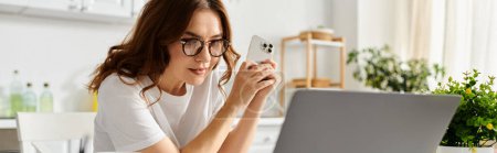Femme d'âge moyen dans des lunettes axées sur l'écran d'ordinateur portable à la maison.