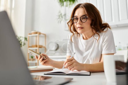 Photo for Middle-aged woman sitting at desk, writing in notebook with pen. - Royalty Free Image