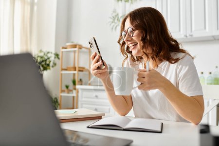 Téléchargez les photos : Femme d'âge moyen tapant sur un ordinateur portable, sirotant une tasse à une table confortable. - en image libre de droit