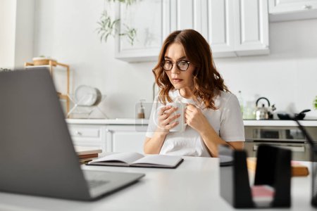 Téléchargez les photos : Femme d'âge moyen immergée dans le travail sur ordinateur portable à la table à la maison. - en image libre de droit