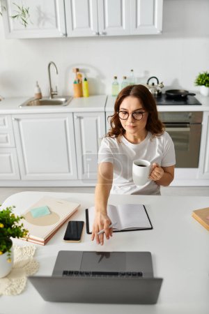 Téléchargez les photos : Femme d'âge moyen travaillant sur un ordinateur portable à une table de cuisine. - en image libre de droit