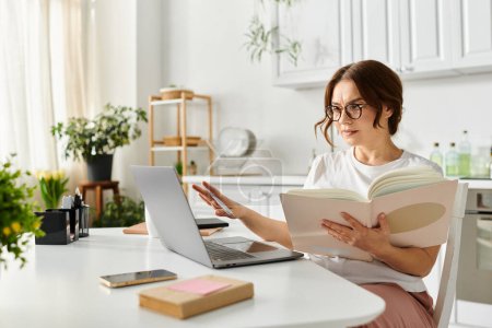 Mujer de mediana edad absorta en un libro, multitarea con un ordenador portátil.