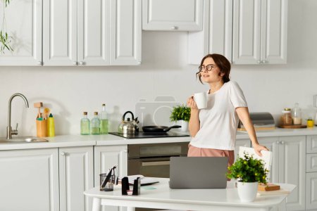 Femme d'âge moyen debout dans la cuisine, tenant une tasse de café.