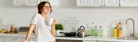 Femme d'âge moyen dégustant une tasse de café dans sa cuisine.