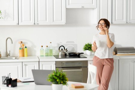 Middle-aged woman standing in a kitchen, talking on a cell phone.