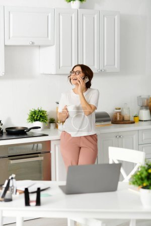 Photo for Middle aged woman on cell phone in kitchen. - Royalty Free Image